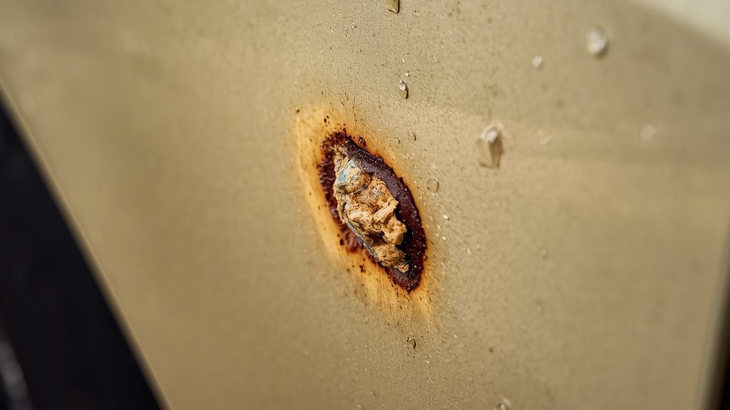 Small paint chip with rust forming on car door panel showing why summer body repair matters in humid Louisiana.